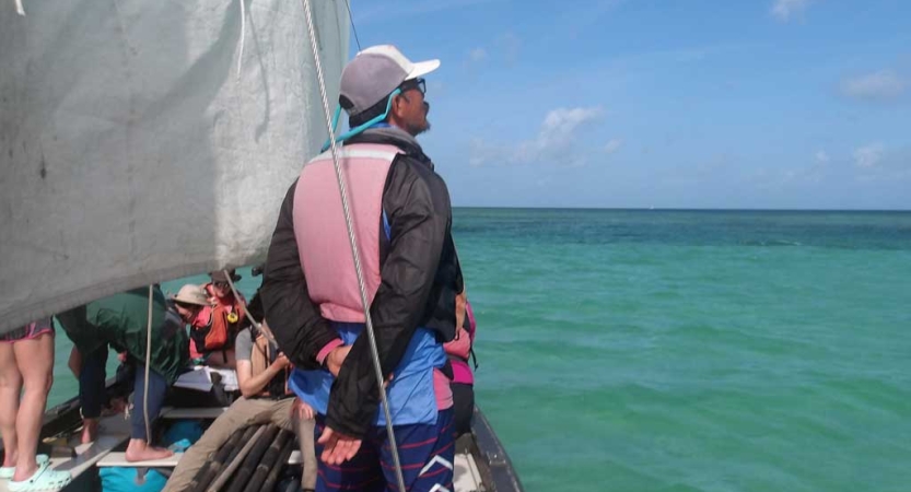 A person wearing a lifejackets stands on a sailboat and looks out over the blue-green water